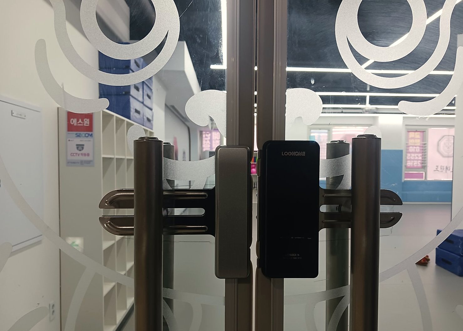 노원구 중계4동 출장 — 무늬 시트를 붙인 유리 양문 가운데에 달린 검은 도어락 본체와 양쪽의 갈색 세로 손잡이